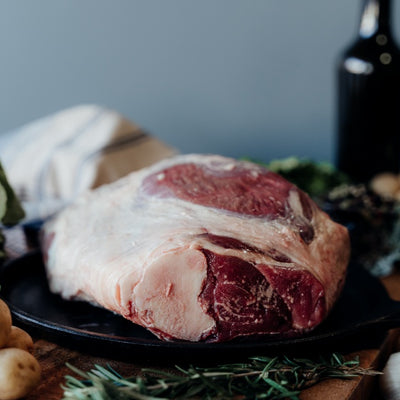 Raw Whole Leg of Lamb on a black skillet with vegetables and a bottle in the background