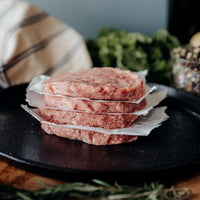 Stack of four raw Lamb patties on a black plate with a rustic background