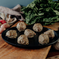 Seven Sugar-Free Adobo Pork Meatballs on a black pan with vegetables and greens in the background