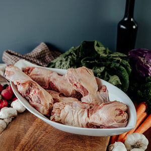 Raw chicken backs on a white plate with vegetables and a bottle on a wooden table
