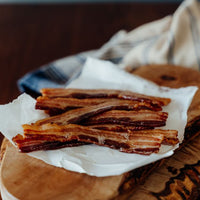 Cooked Sugar Free Pork Bacon Slices on a wooden cutting board with a cloth underneath