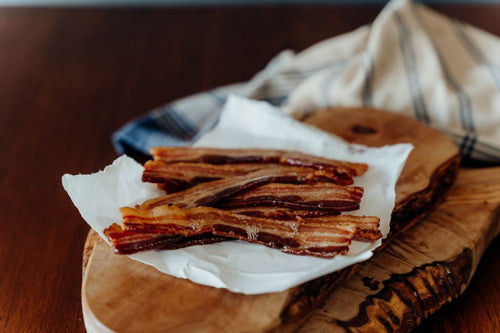 Cooked Sugar Free Pork Bacon Slices on a wooden cutting board with a cloth underneath